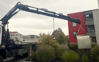 Ein Baukrank hievt eine Wärmepumpe durch die Luft an ihren neuen Standort.