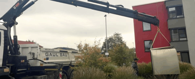 Ein Baukrank hievt eine Wärmepumpe durch die Luft an ihren neuen Standort.